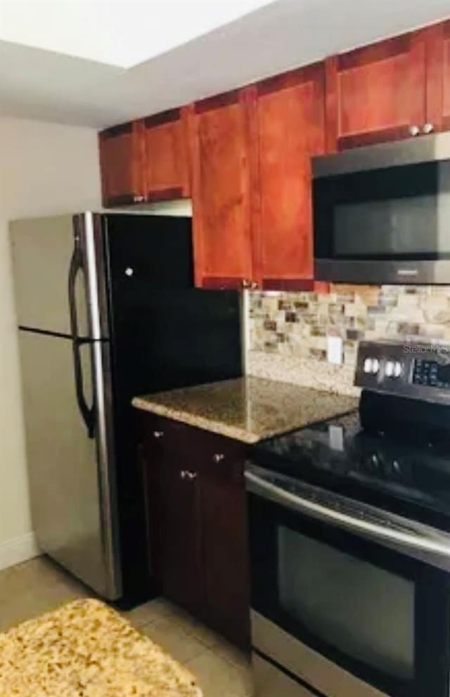 kitchen with decorative backsplash, appliances with stainless steel finishes, light tile patterned flooring, and light stone countertops