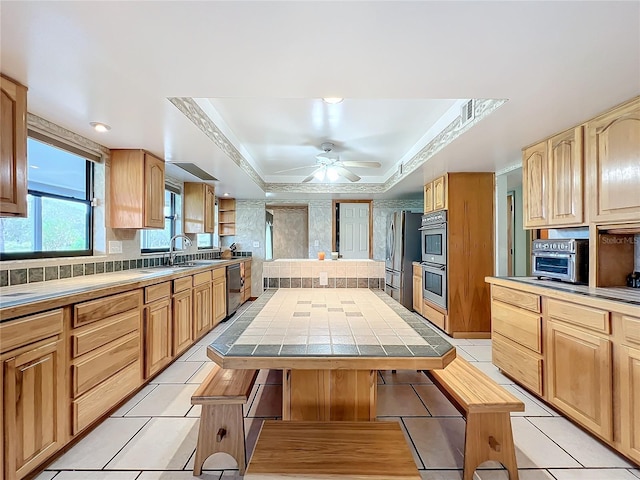 kitchen featuring stainless steel appliances, ceiling fan, a tray ceiling, a center island, and tile counters