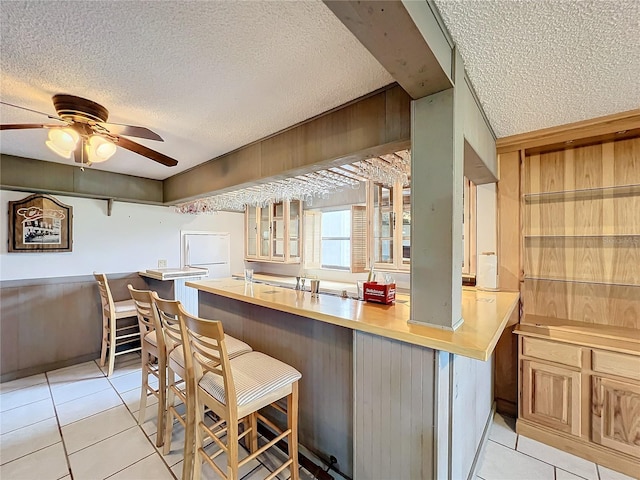 kitchen featuring a textured ceiling, light tile patterned floors, a breakfast bar, kitchen peninsula, and ceiling fan