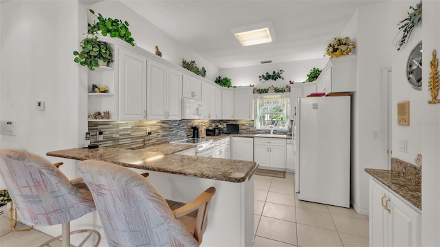 kitchen with kitchen peninsula, a breakfast bar area, white appliances, white cabinets, and decorative backsplash