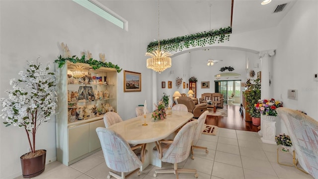 tiled dining room with a high ceiling and ceiling fan with notable chandelier