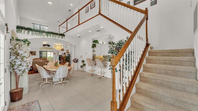 stairs featuring a towering ceiling, tile patterned flooring, and an inviting chandelier