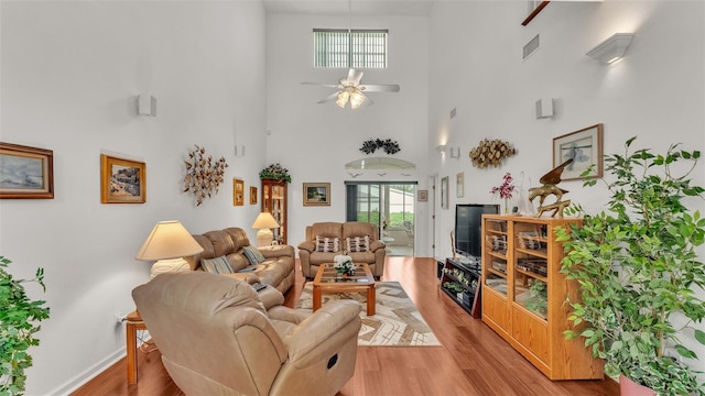 living room featuring a towering ceiling, ceiling fan, light hardwood / wood-style flooring, and french doors