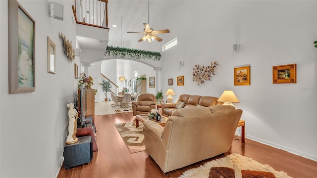 living room featuring a high ceiling, light wood-type flooring, decorative columns, and ceiling fan with notable chandelier