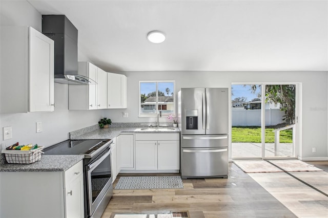 kitchen featuring stainless steel appliances, wall chimney range hood, sink, light hardwood / wood-style floors, and white cabinetry