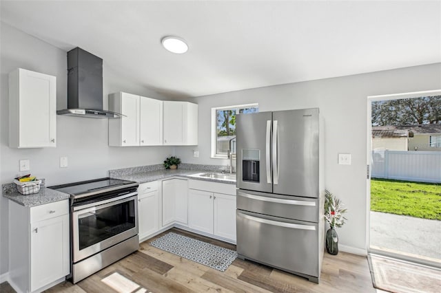 kitchen featuring appliances with stainless steel finishes, sink, wall chimney range hood, light hardwood / wood-style flooring, and white cabinetry