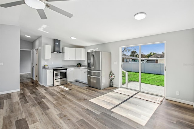 kitchen featuring white cabinetry, ceiling fan, stainless steel appliances, wall chimney range hood, and light hardwood / wood-style flooring