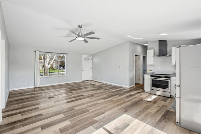 kitchen featuring wall chimney exhaust hood, ceiling fan, white refrigerator, light hardwood / wood-style floors, and stainless steel electric range