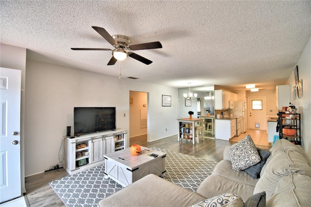 living room with a textured ceiling, ceiling fan with notable chandelier, and light hardwood / wood-style flooring