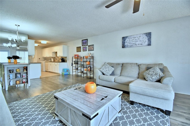 living room featuring ceiling fan with notable chandelier, dark wood-type flooring, and a textured ceiling