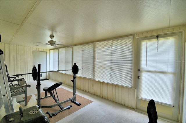 exercise room with wood walls, ceiling fan, and a textured ceiling