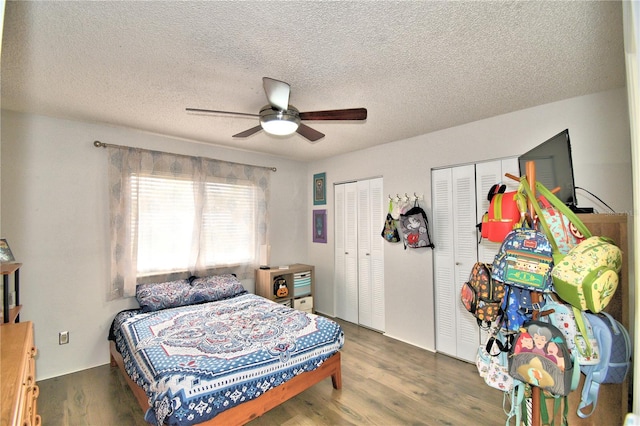 bedroom with dark wood-type flooring, a textured ceiling, ceiling fan, and multiple closets