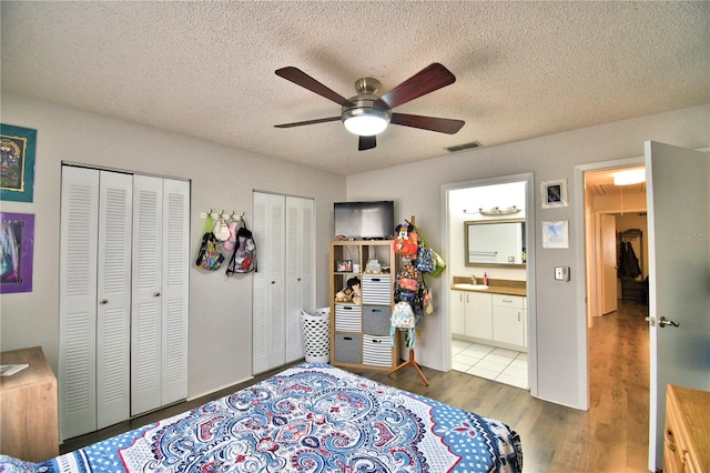 bedroom featuring sink, ceiling fan, wood-type flooring, connected bathroom, and two closets