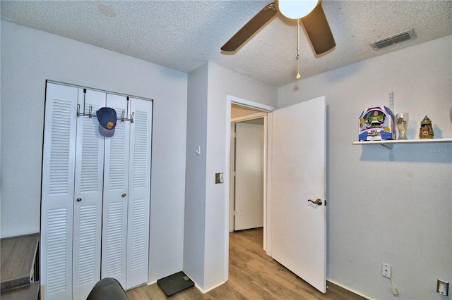 bedroom with light hardwood / wood-style floors, ceiling fan, a textured ceiling, and a closet