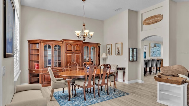 dining space with a chandelier, a towering ceiling, and light hardwood / wood-style flooring