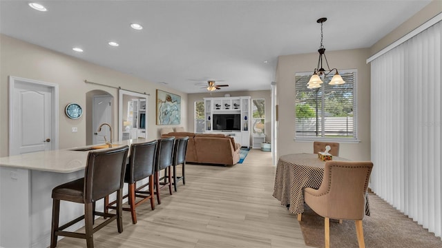 dining room with ceiling fan with notable chandelier, sink, and light hardwood / wood-style flooring