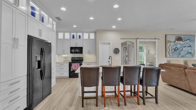 kitchen with a kitchen breakfast bar, light hardwood / wood-style flooring, an island with sink, white cabinets, and black appliances