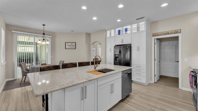 kitchen with light stone counters, a kitchen island with sink, sink, black appliances, and white cabinets