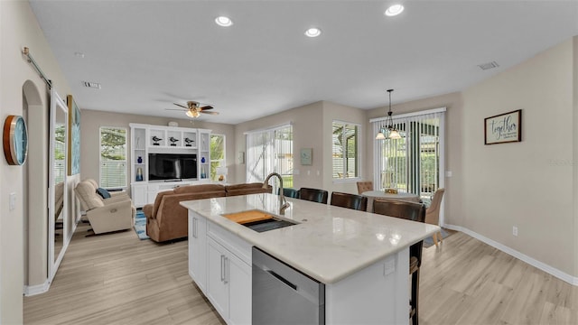 kitchen featuring pendant lighting, a kitchen island with sink, sink, stainless steel dishwasher, and light wood-type flooring