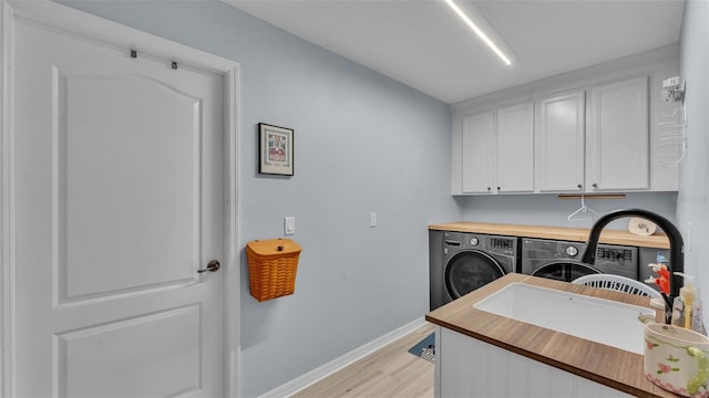 clothes washing area featuring cabinets, independent washer and dryer, sink, and light hardwood / wood-style flooring