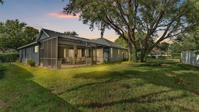 back house at dusk featuring a lanai, a patio area, and a lawn