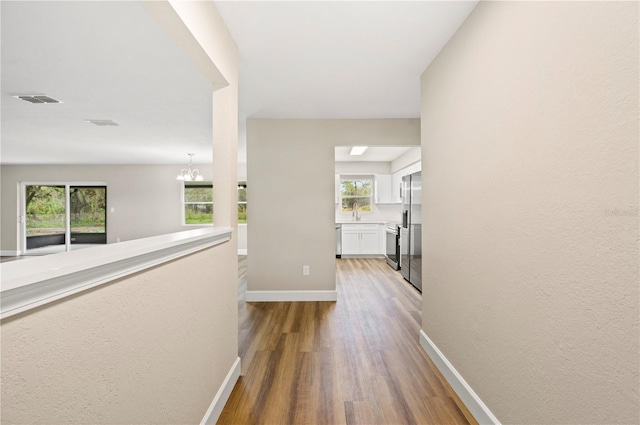 hall with an inviting chandelier, wood-type flooring, and a healthy amount of sunlight