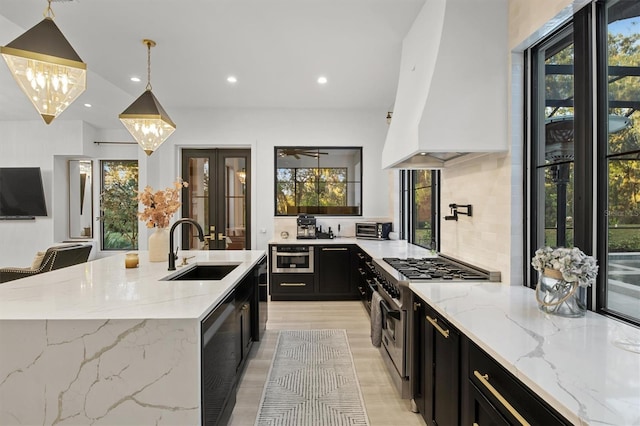 kitchen featuring sink, a kitchen island with sink, light stone countertops, pendant lighting, and high end stove