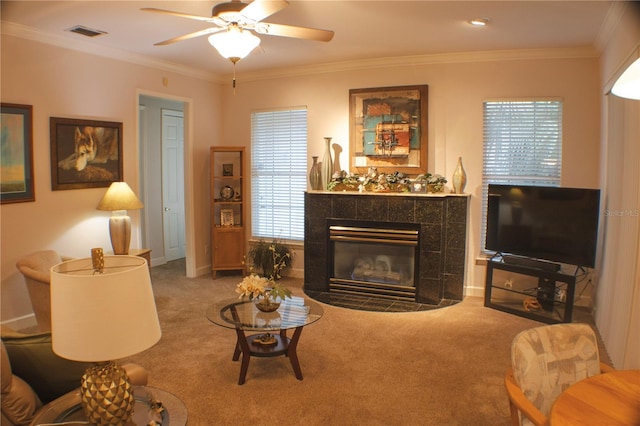 carpeted living room with ceiling fan, a tiled fireplace, and ornamental molding