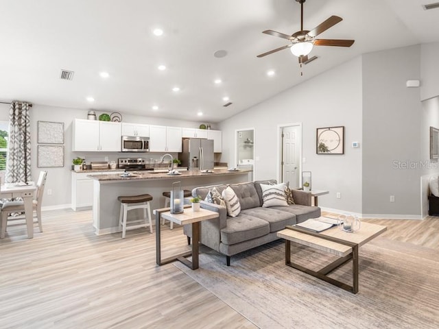 living room featuring light wood-type flooring, ceiling fan, sink, and high vaulted ceiling