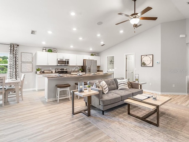 living room featuring light wood-type flooring, ceiling fan, sink, and high vaulted ceiling