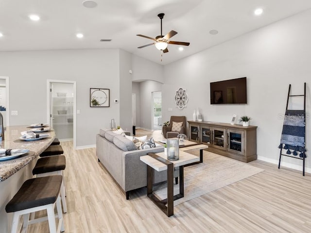 living room with light wood-type flooring, ceiling fan, and high vaulted ceiling