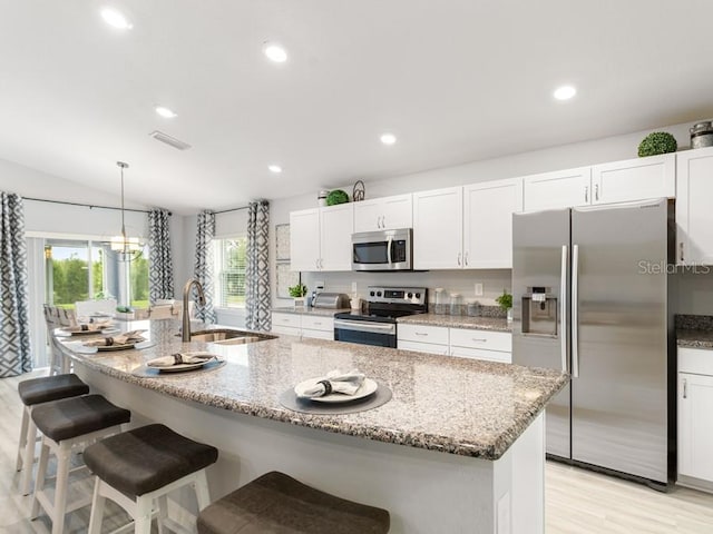 kitchen featuring white cabinetry, appliances with stainless steel finishes, decorative light fixtures, and an island with sink