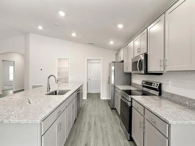 kitchen featuring an island with sink, vaulted ceiling, a sink, arched walkways, and appliances with stainless steel finishes