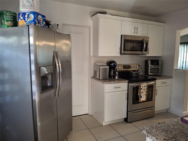 kitchen with light tile patterned flooring, white cabinetry, appliances with stainless steel finishes, light stone countertops, and decorative backsplash