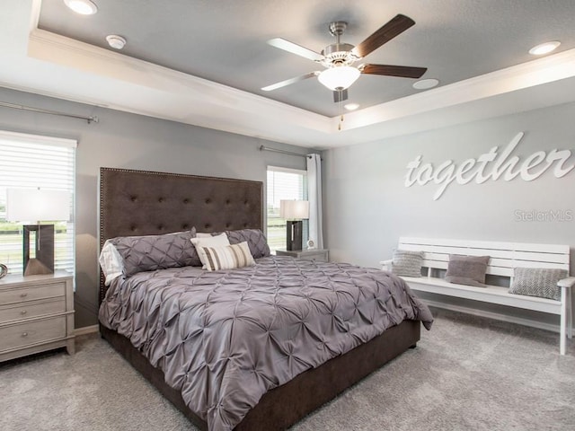 carpeted bedroom featuring ornamental molding, multiple windows, a raised ceiling, and ceiling fan