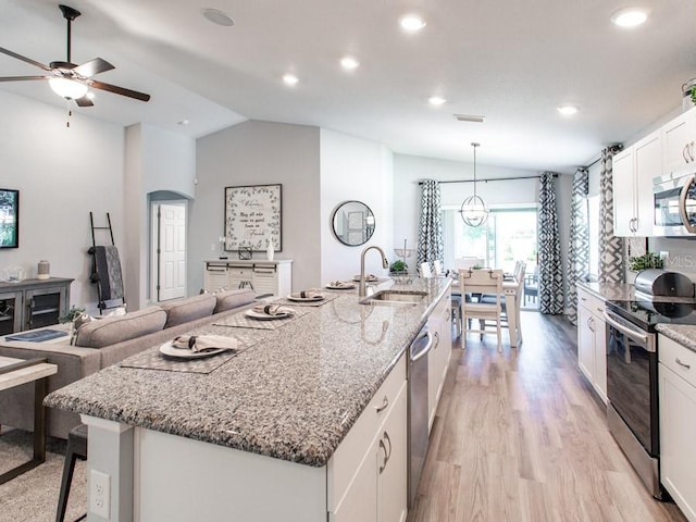 kitchen with lofted ceiling, white cabinets, an island with sink, pendant lighting, and appliances with stainless steel finishes