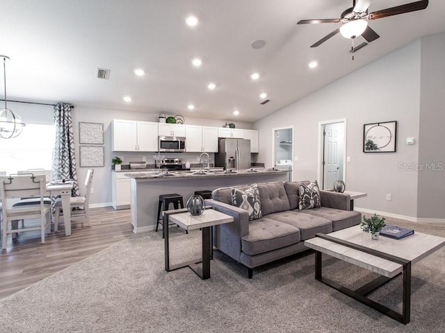 living room with ceiling fan with notable chandelier, light hardwood / wood-style flooring, lofted ceiling, and sink