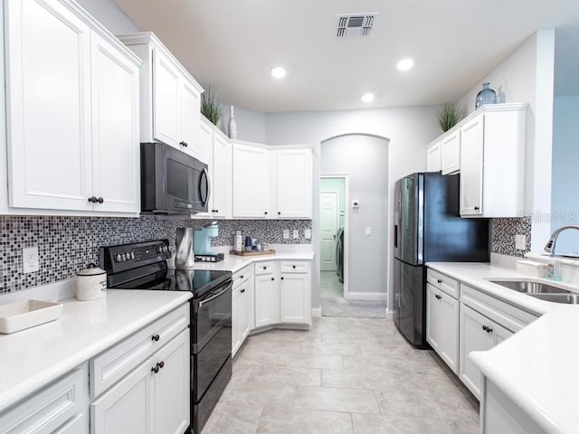 kitchen with decorative backsplash, black appliances, sink, white cabinetry, and washer / dryer