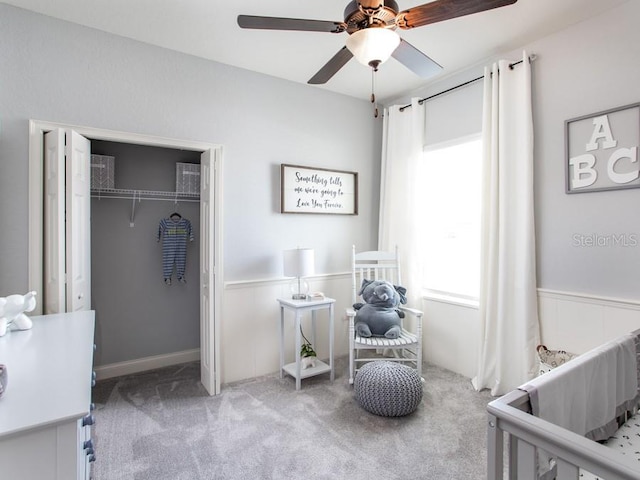 carpeted bedroom with a nursery area, ceiling fan, and a closet