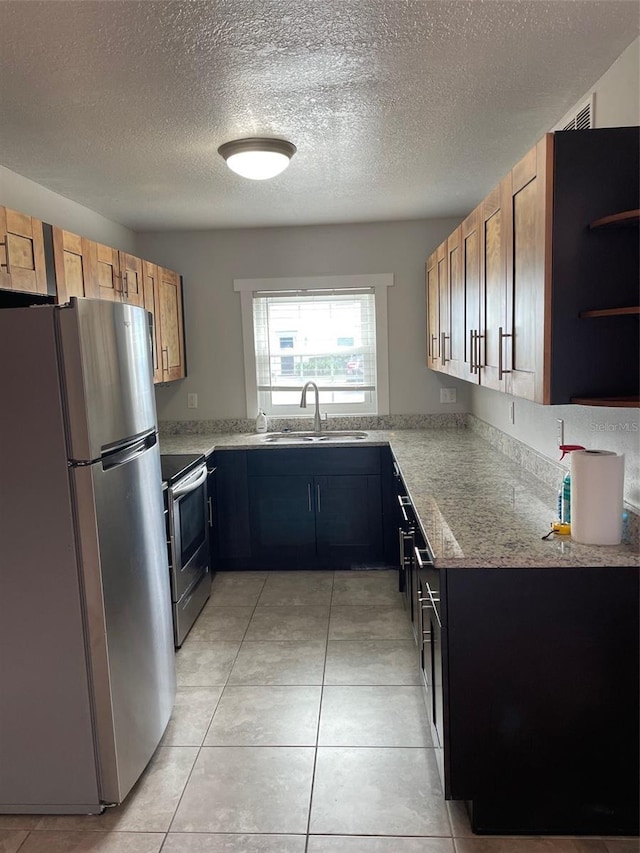 kitchen featuring sink, light stone counters, a textured ceiling, light tile patterned floors, and appliances with stainless steel finishes