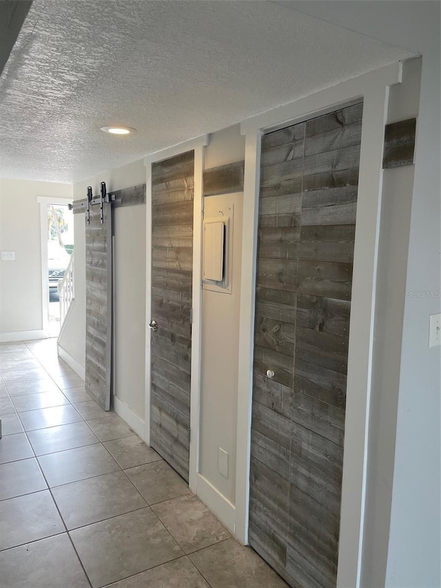 corridor with a textured ceiling, a barn door, and light tile patterned flooring