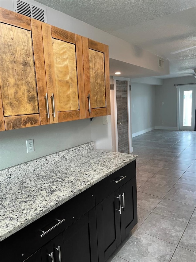 kitchen featuring ceiling fan, light stone counters, light tile patterned floors, and a textured ceiling