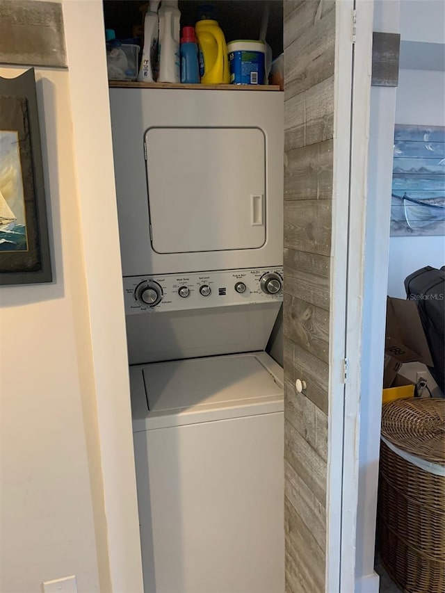 clothes washing area with wooden walls and stacked washer and clothes dryer