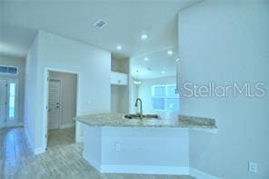 kitchen with white cabinets, light hardwood / wood-style floors, light stone counters, and kitchen peninsula