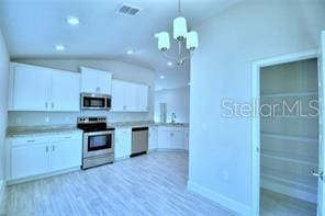 kitchen featuring stainless steel appliances, white cabinetry, decorative light fixtures, light wood-type flooring, and vaulted ceiling