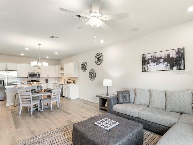 living room with ceiling fan with notable chandelier and light hardwood / wood-style flooring