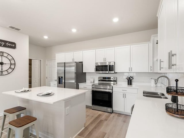 kitchen with light wood-type flooring, white cabinetry, a kitchen island, and appliances with stainless steel finishes