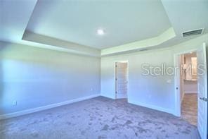 unfurnished bedroom featuring carpet flooring and a tray ceiling