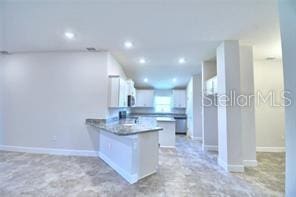 kitchen with white cabinets, dark stone counters, and kitchen peninsula