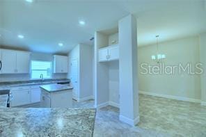 kitchen with white cabinetry, pendant lighting, light stone counters, and a center island